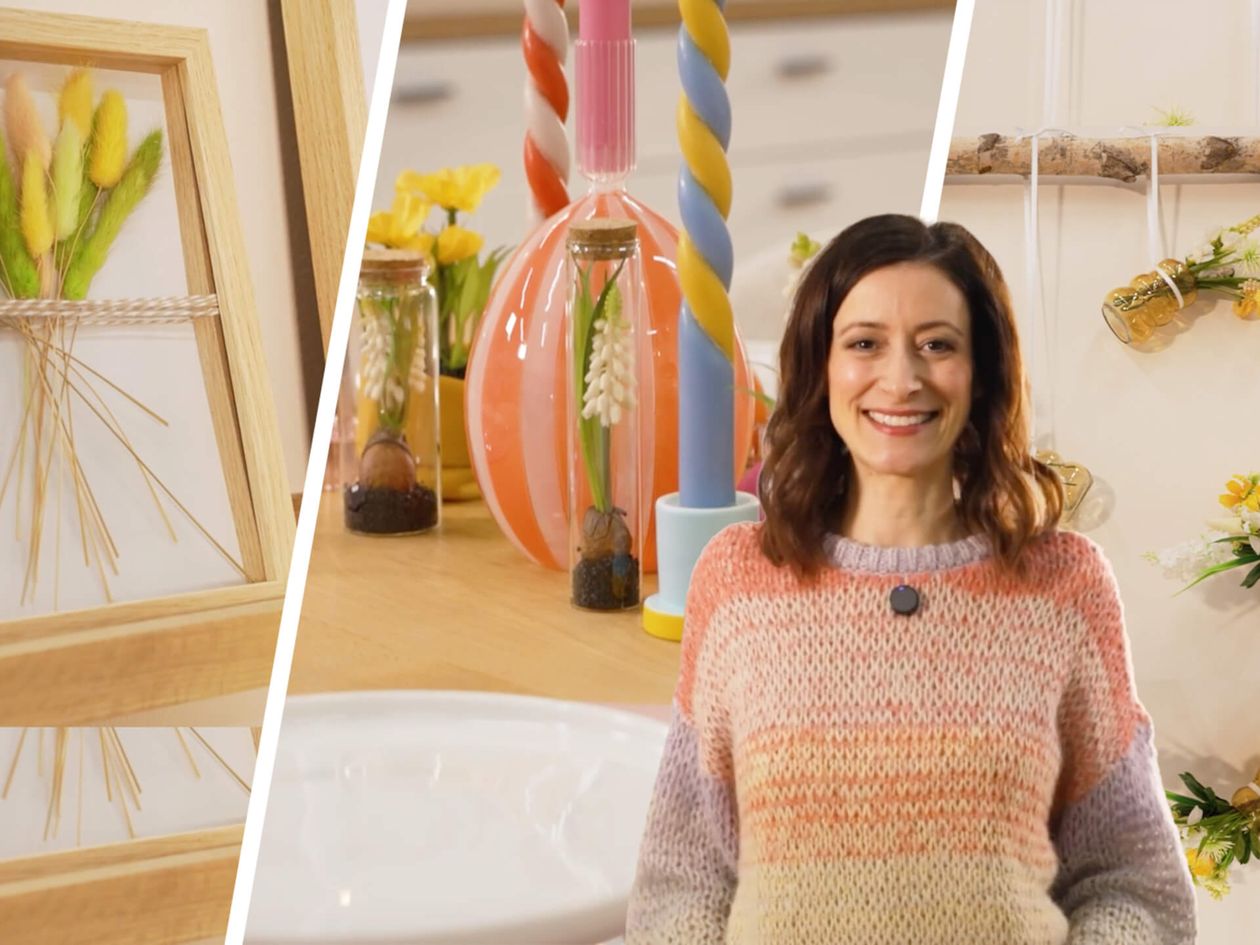 Eine Frau in einem bunten Pullover steht in einem farbenfrohen Raum, in dessen Hintergrund Kunsthandwerk, dekorative Gläser und ein geometrisches Kunstwerk aus Holz zu sehen sind.