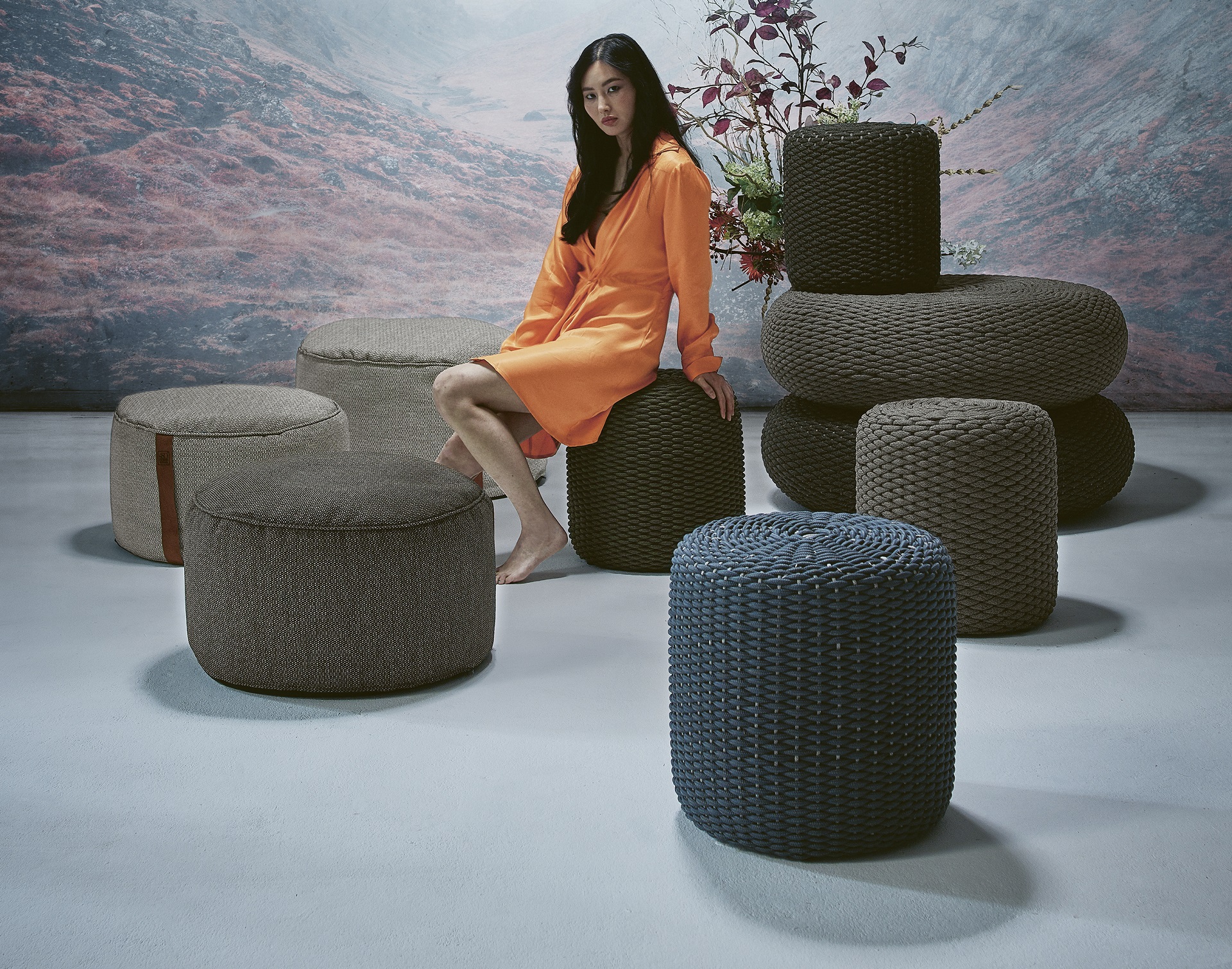 Gartenhocker Liten aus dem Hause Idyl in Anthrazit und einer runden Form in Aufstellung mit verschiedenen anderen Hockern und einer Frau in orangenem Kleid