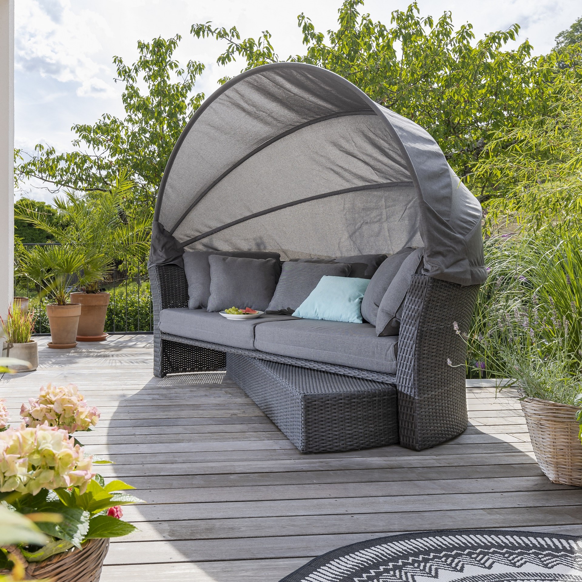 Sonneninsel Deluxe aus grauem Geflecht mit einfahrbaren Liegen auf einer sommerlichen Terrasse