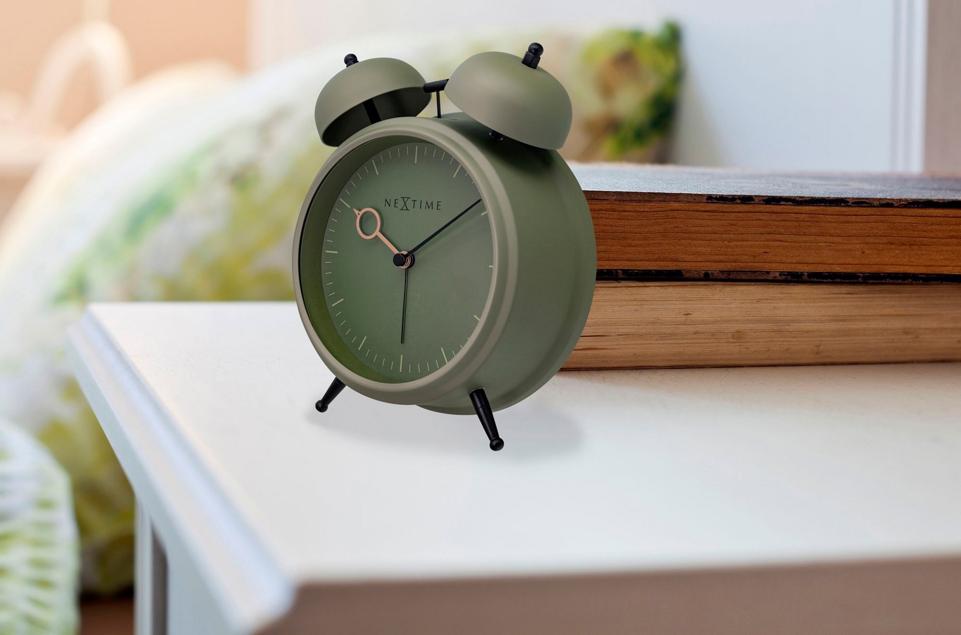 Analoger Quarzwecker Golden Hour der Marke Nextime aus Alu, Eisen, Stahl und Metall auf einem Nachtkästchen mit Bett im Hintergrund