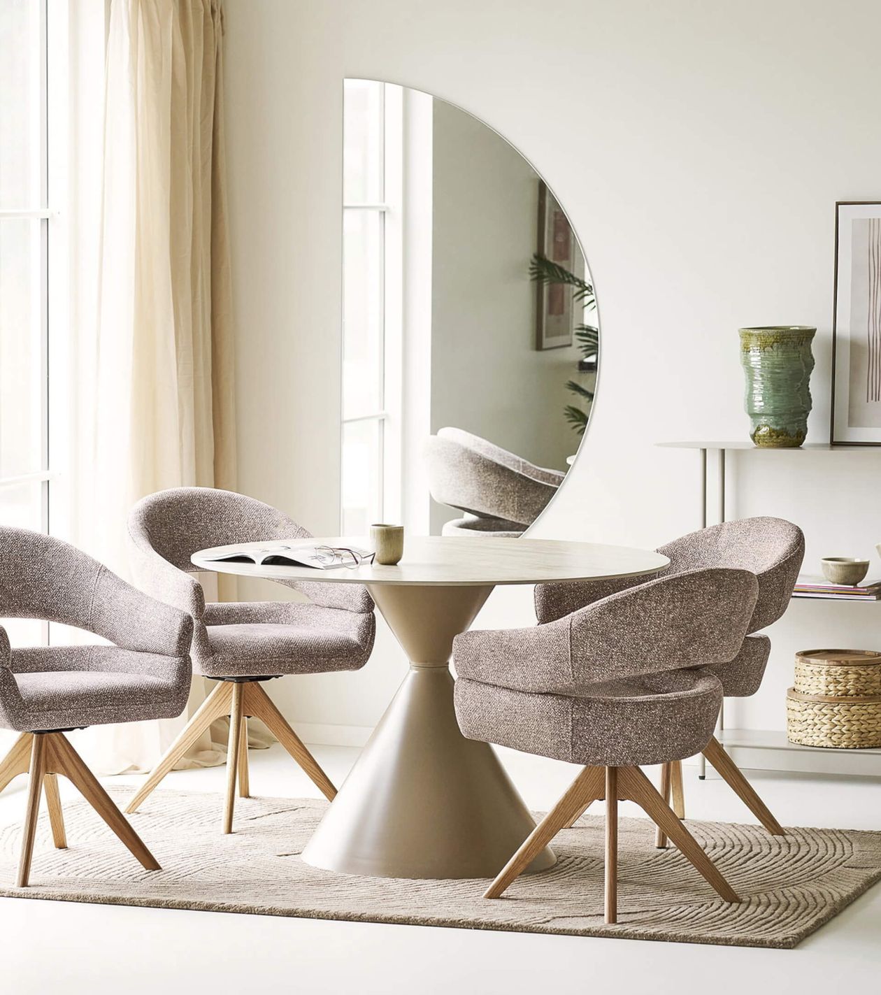 Moderner Essbereich mit rundem Tisch, vier gepolsterten Stühlen, großem halbkreisförmigem Spiegel, grüner Vase und pastellfarbenem Dekor.
