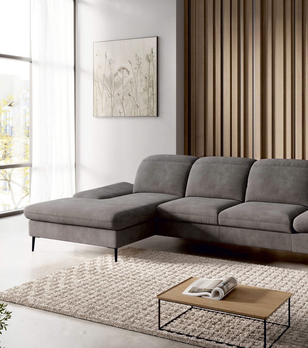 Modernes Wohnzimmer mit grauem Ecksofa, hellem Teppich, Holz-Couchtisch, großem Fenster und einem Wandbild mit Pflanzenmotiv.