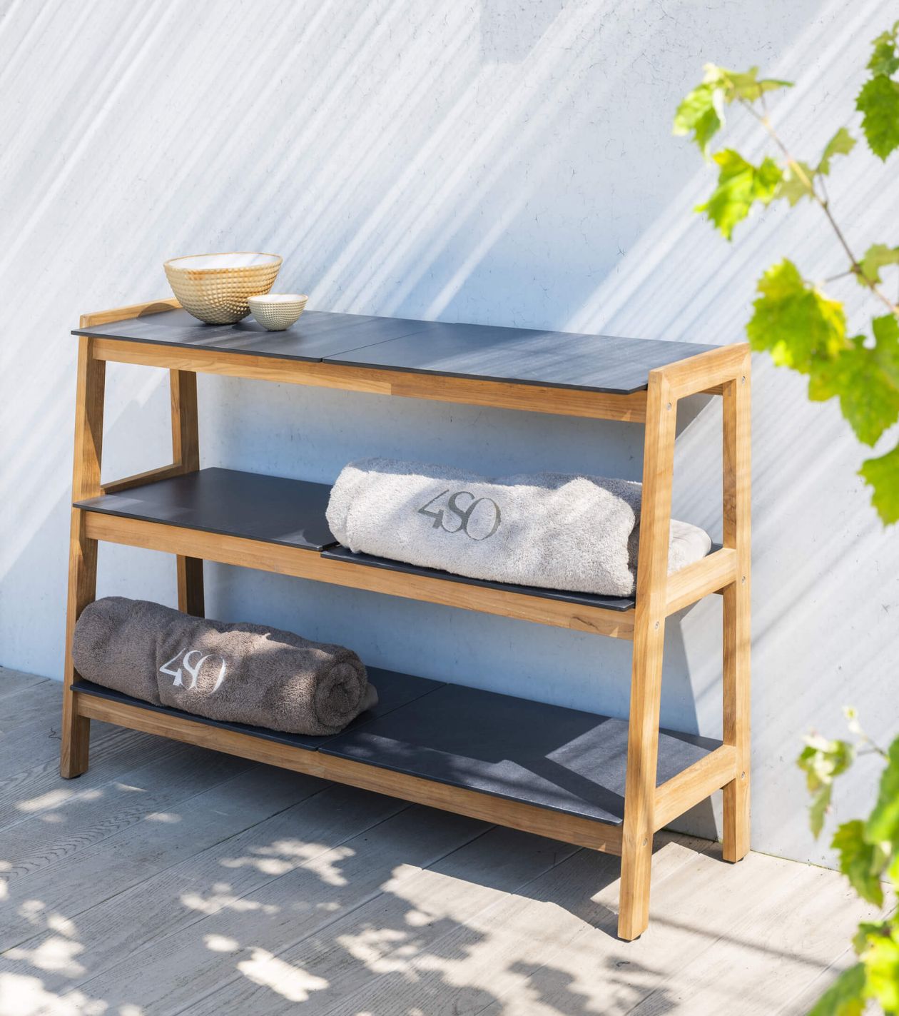 Holzregal mit schwarzem Regalboden, darauf zwei Schalen. Darunter zwei gerollte Handtücher mit "450"-Aufschrift. Sonnenlicht streift die Szene.