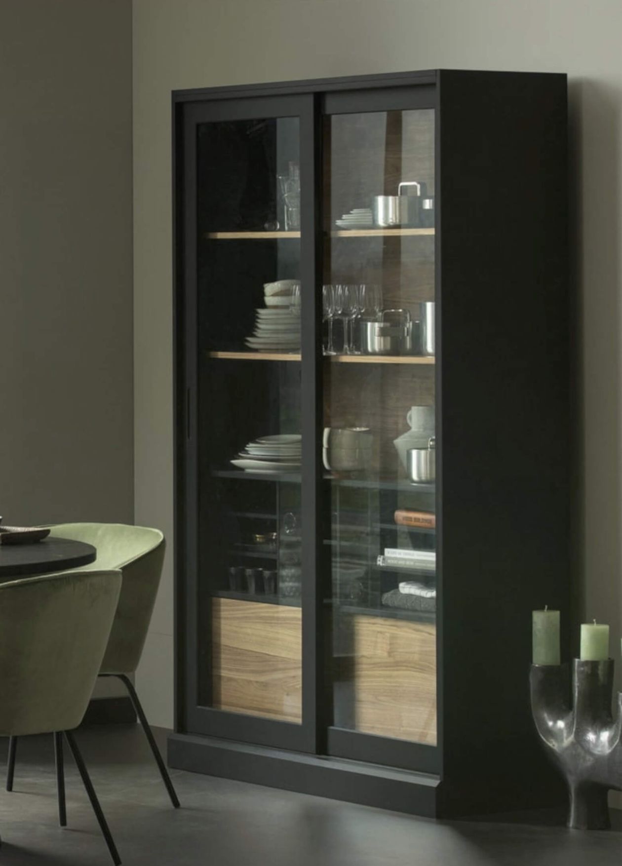 Ein Regal mit Büchern, einem schwarzen Mannequin-Kopf, Dekoartikeln und Keramik darauf. Links ist teilweise ein Wandbild aus Metall zu sehen.