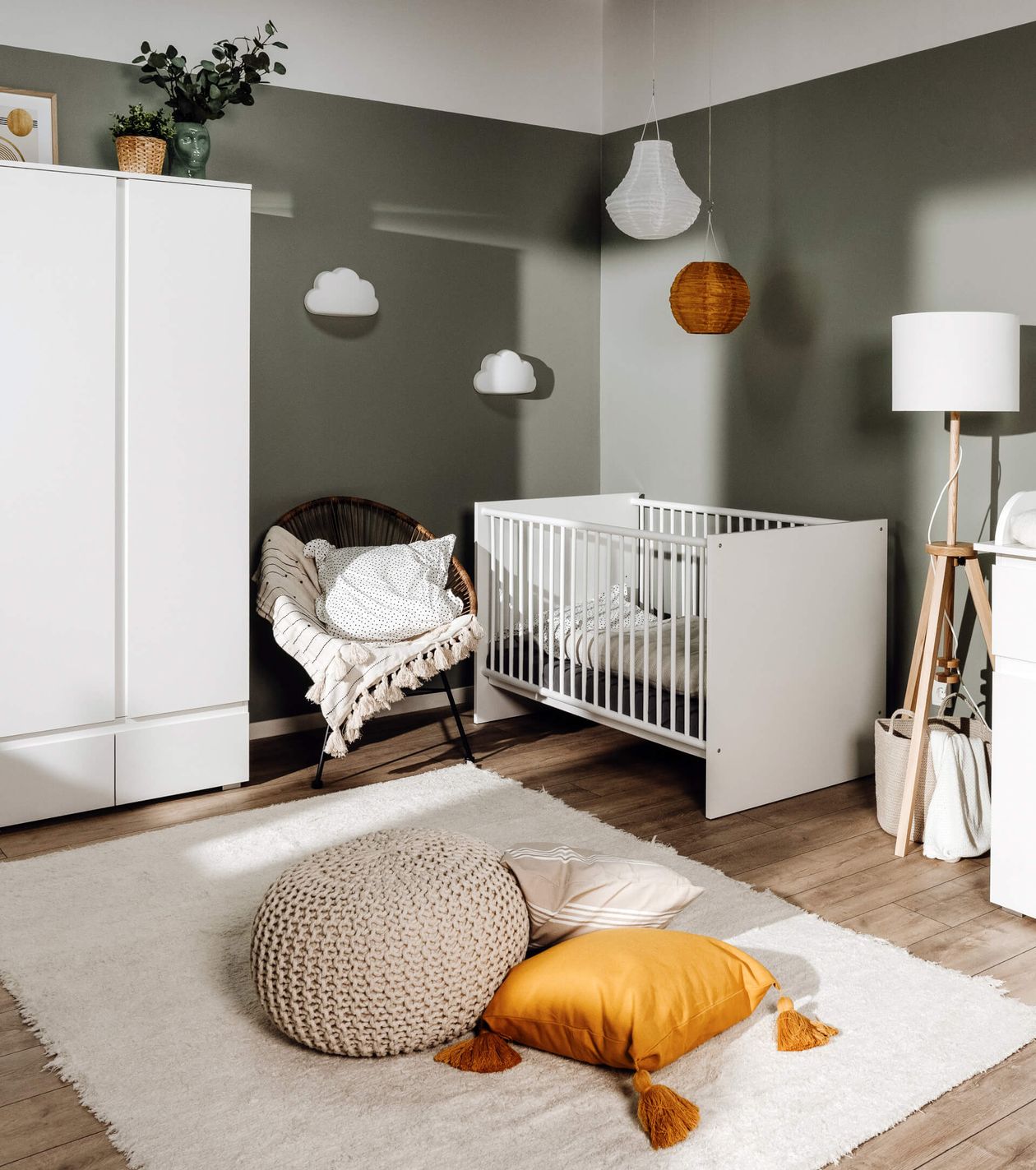 Modernes Kinderzimmer mit weißem Gitterbett, grünem Stuhl, gelbem Kissen, weißem Teppich, pastellgrüner Wand und Wolkendekor.