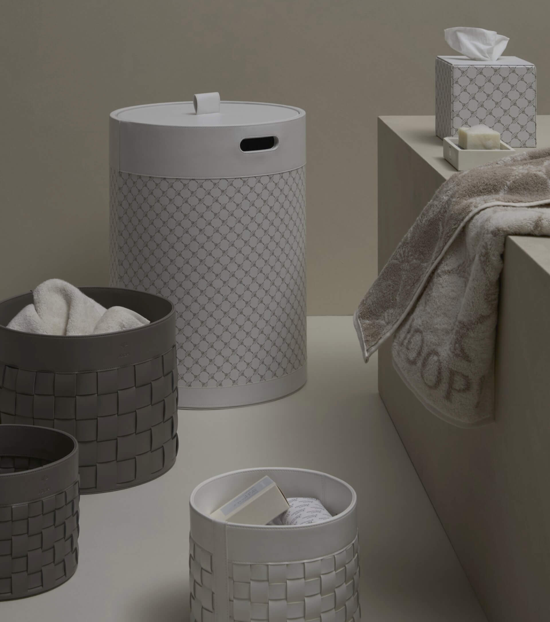 Badezimmerszene mit geflochtenen Körben, einem Wäschekorb, einem Handtuch, Taschentüchern und Seife auf einer beigen Oberfläche. Neutrale Farbtöne dominieren die Umgebung.