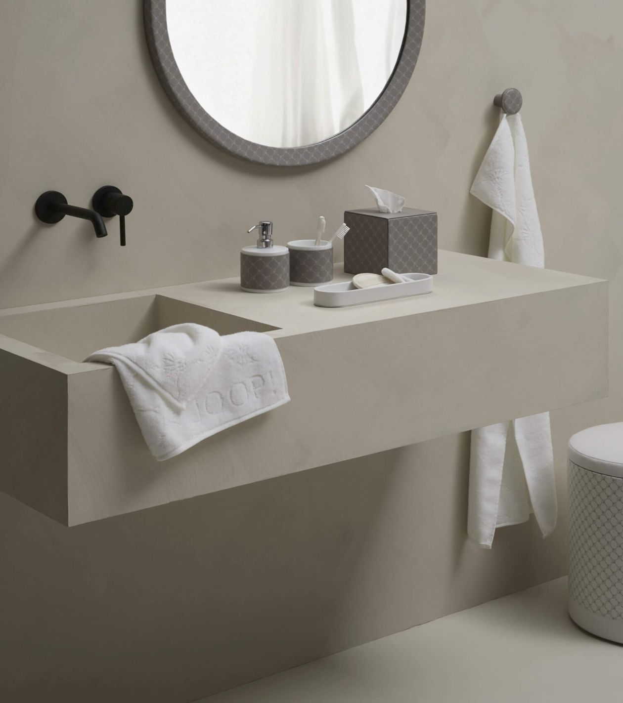 Modern bathroom with beige sink, round mirror, black faucet, and stylish accessories, including towels and toiletries on the counter.