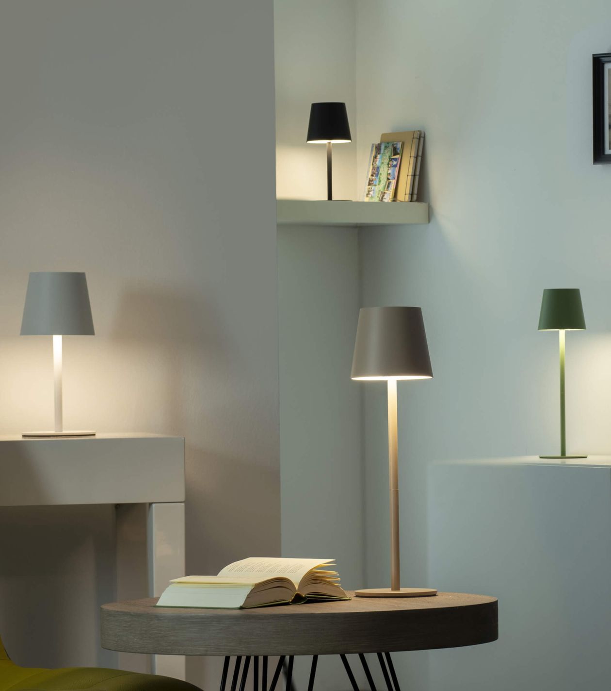 Ein modernes Zimmer mit eleganten Tischlampen auf einem Schreibtisch und einem Regal, einem aufgeschlagenen Buch auf einem runden Tisch und einer minimalistischen Einrichtung.