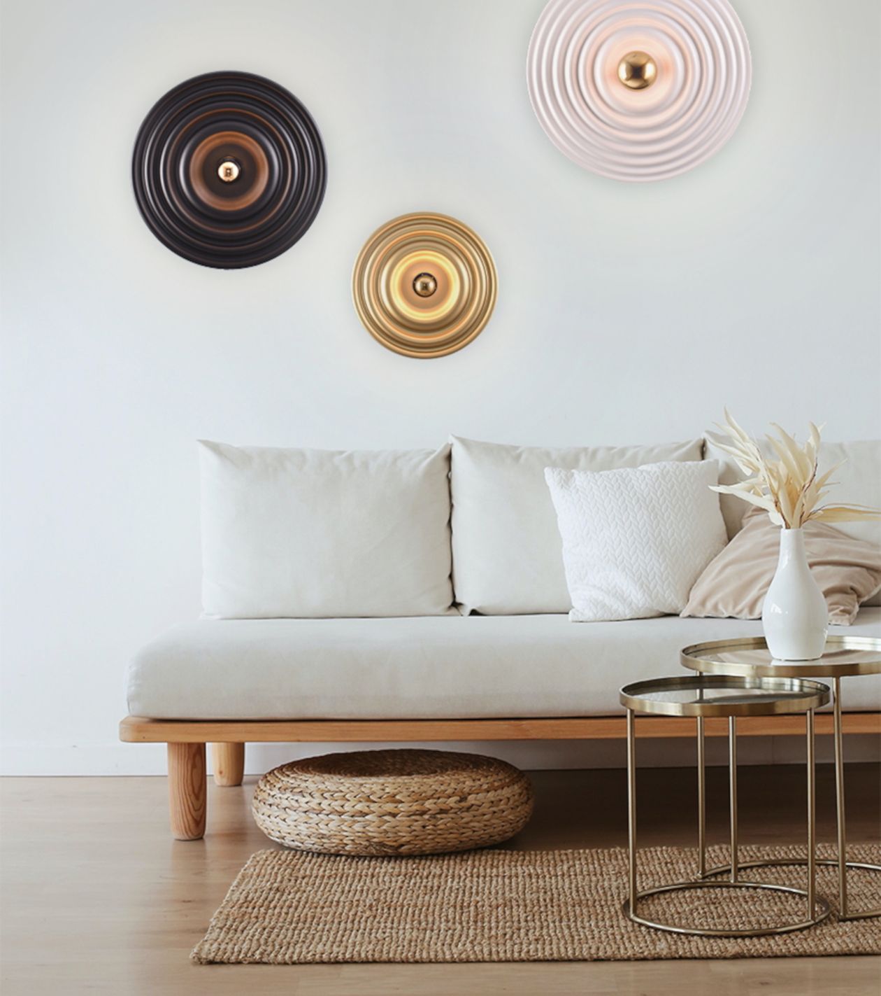 Modernes Wohnzimmer mit weißem Sofa, runden Couchtischen, Korbhocker und drei dekorativen runden Wandleuchten in Schwarz, Gold und Weiß.