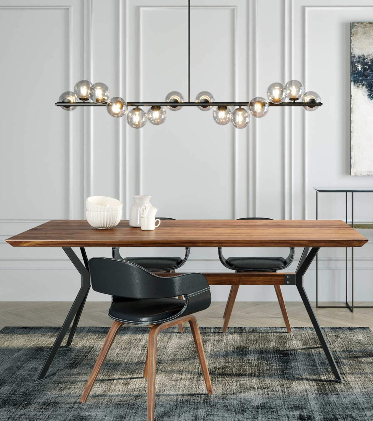 Moderner Essbereich mit einem Holztisch, zwei schwarzen Stühlen, einem einzigartigen Kronleuchter und Dekorationsartikeln auf dem Tisch. Weiße Wandvertäfelung im Hintergrund.