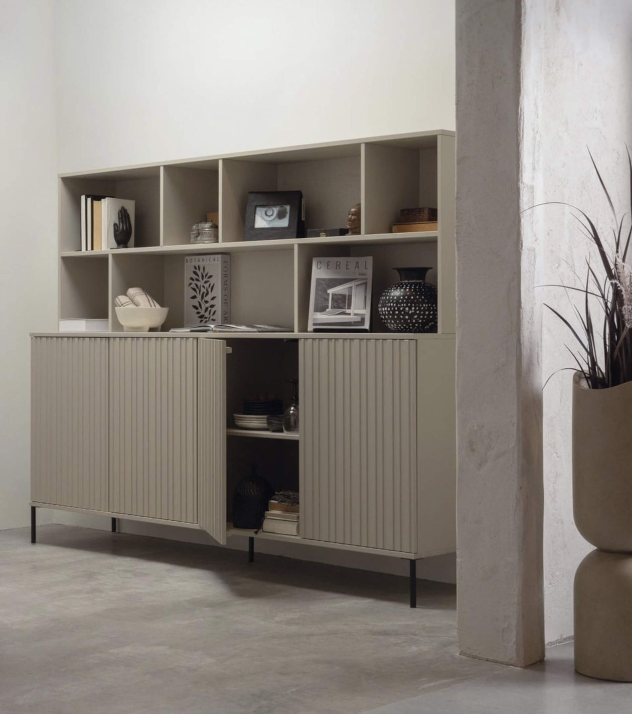 Wandschrank in hellgrau mit Lamellen-Türen. Daneben eine betonierte Wand und ein Blumentopf.