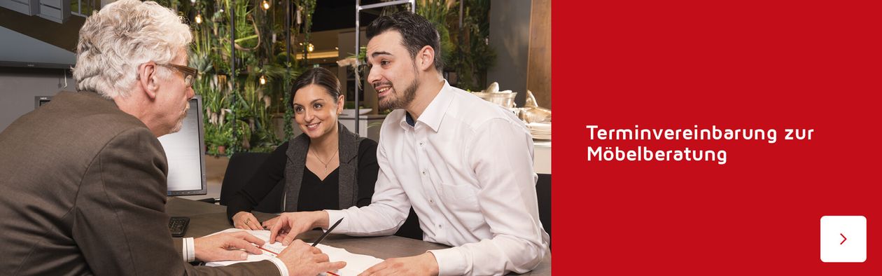 Drei Personen diskutieren an einem Tisch in einem modernen Büro über Dokumente. Text lautet „Terminvereinbarung zur Möbelberatung“.