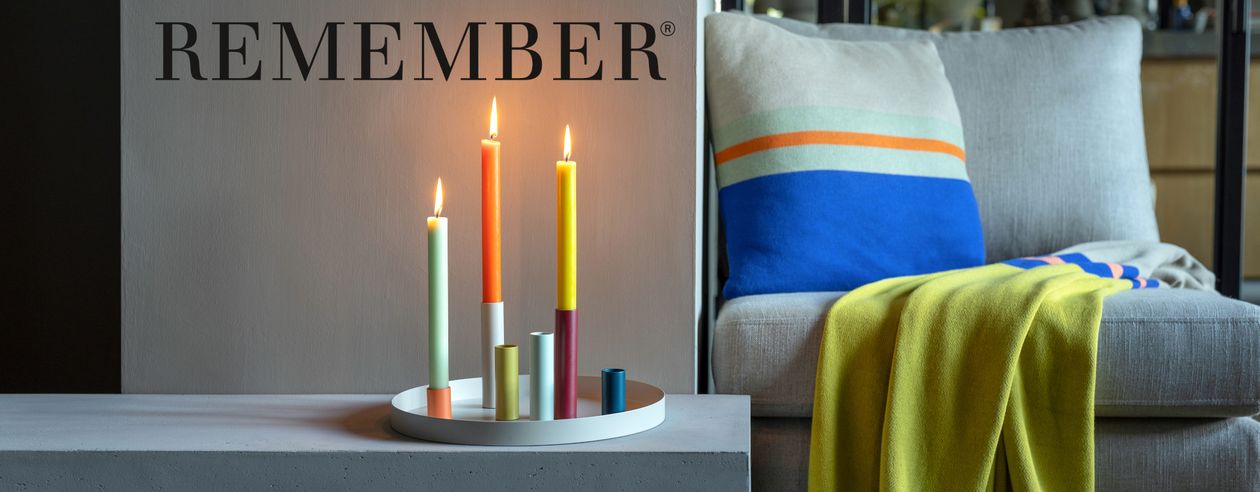 Drei farbige Kerzen stecken in den magnetischen Kerzenhaltern des Kerzenleuchters Luna. Im Hintergrund ist ein gemütlicher Sessel zu sehen.