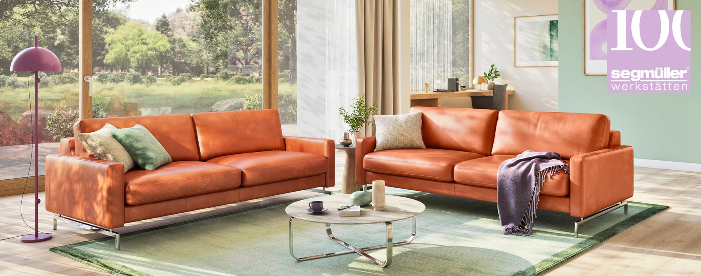Modernes Wohnzimmer mit zwei orangefarbenen Ledersofas, einem runden Couchtisch aus Glas und einer violetten Stehlampe. Große Fenster bieten einen Blick auf den Garten.