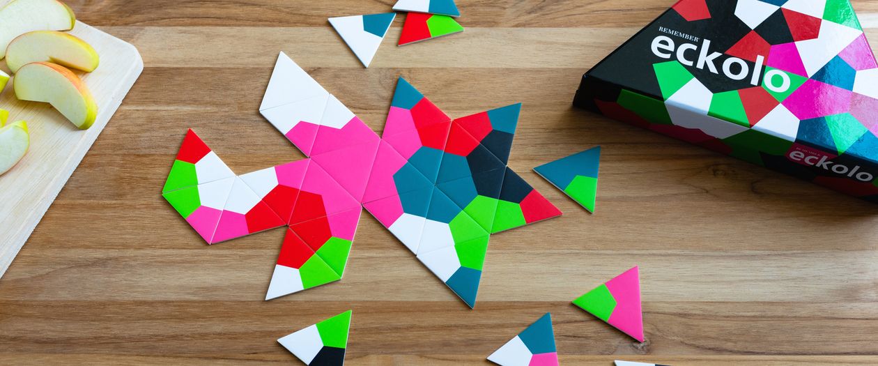 Die Box und bunte Spielsteine der Spiels Spiel Eckolo von Remember liegen auf einem Holztisch.