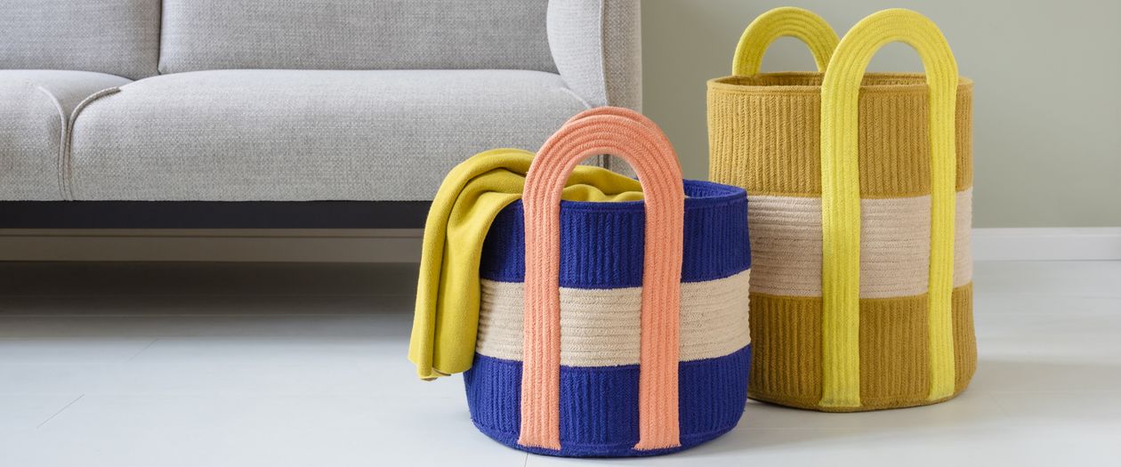 Ein blauer und ein gelber Baumwollkorb des Modells Colombo aus dem Hause Remember stehen vor einem Skandi-Sofa..