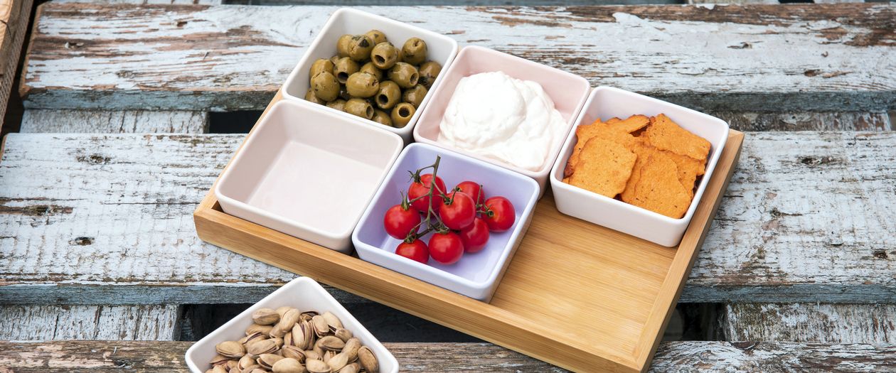 Das in unauffälligen Farben gehaltenen siebenteilige Schalenset Bambus von Remember liegt auf einem Holztisch. Die Schalen sind mit verschiedenen Snacks gefüllt.
