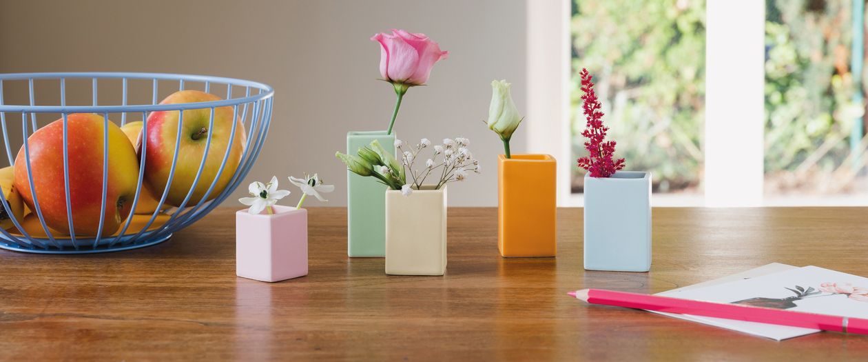 Das fünfteilige, in Pastellfarben gehaltenen Vasenset Mini von Remember steht auf einem Holztisch. Die zylindrischen Vasen sind mit verschiedenen Blumen gefüllt.