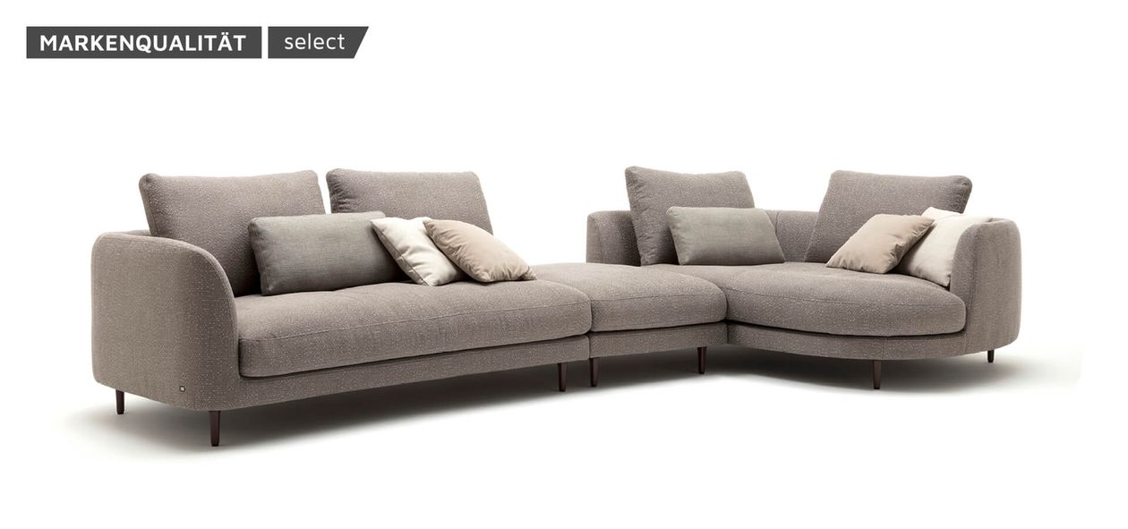 Modernes graues Ecksofa mit mehreren Kissen, stromlinienförmigem Design und leicht erhöhten, schlanken Beinen.