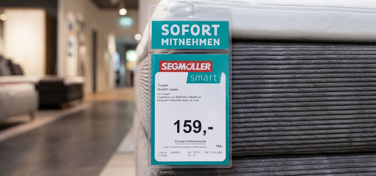 Auf dem Preisschild einer Matratze in einem Geschäft steht „159,-“ unter der Linie „Segmüller smart“. Darüber steht „Sofort mitnehmen“.