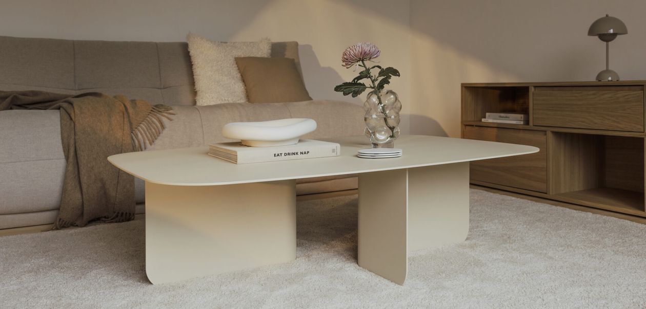 Minimalistisches Wohnzimmer mit einem beigen Couchtisch, Büchern und einer Vase mit einer Blume. Sofa und Holzschrank im Hintergrund.