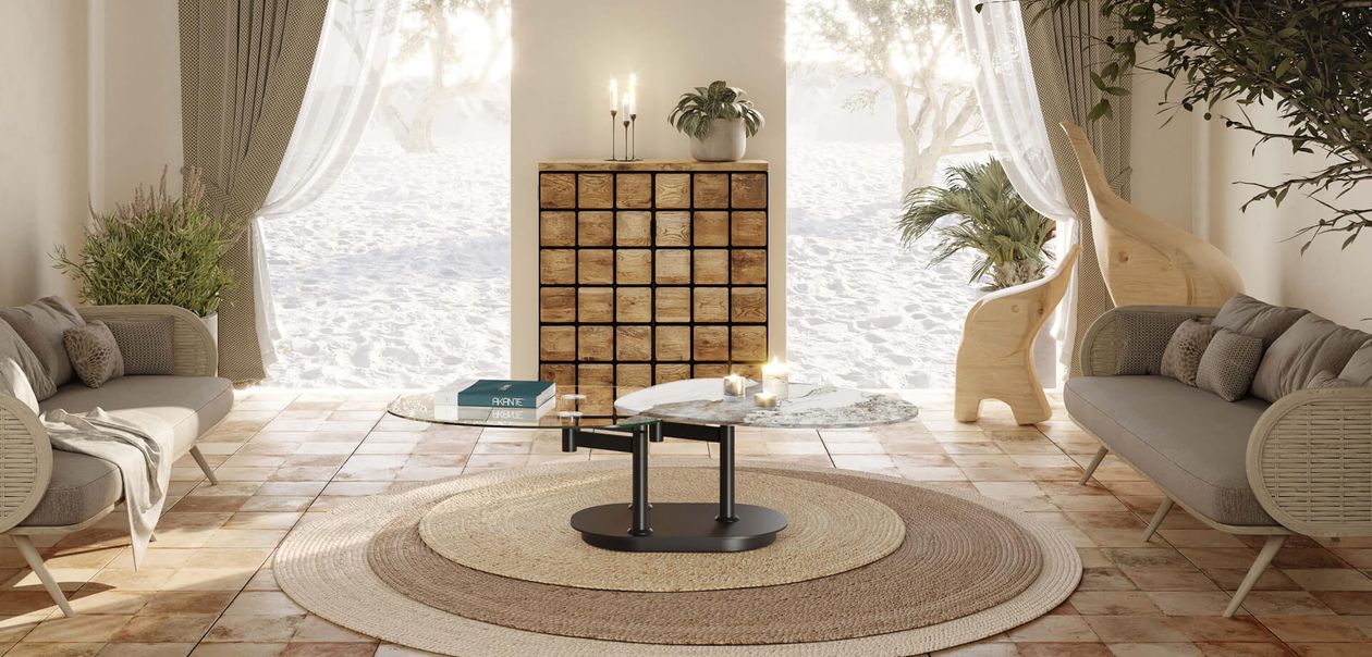 Ein gemütliches Wohnzimmer mit zwei grauen Sofas, einem runden Teppich, einem Couchtisch aus Glas und einem Holzschrank. Große Fenster bieten einen Blick auf die sandige Außenlandschaft.