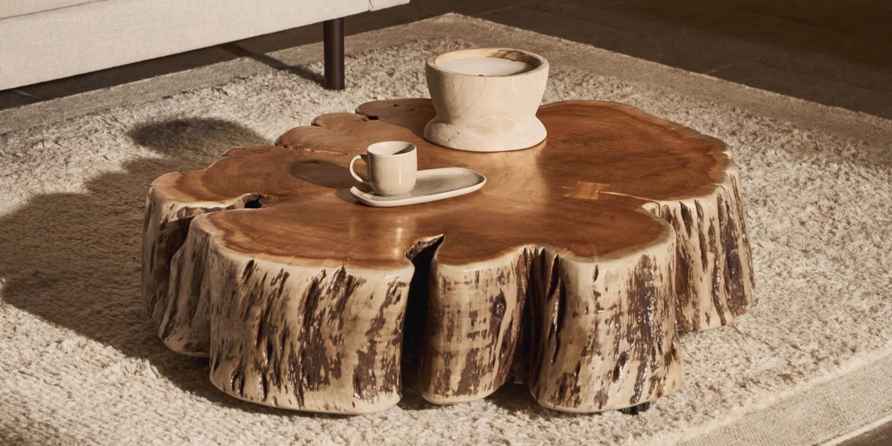 Ein rustikaler Couchtisch aus einem Baumstamm mit natürlicher Oberfläche, auf dem eine Tasse und eine Schale stehen, auf einem strukturierten Teppich.