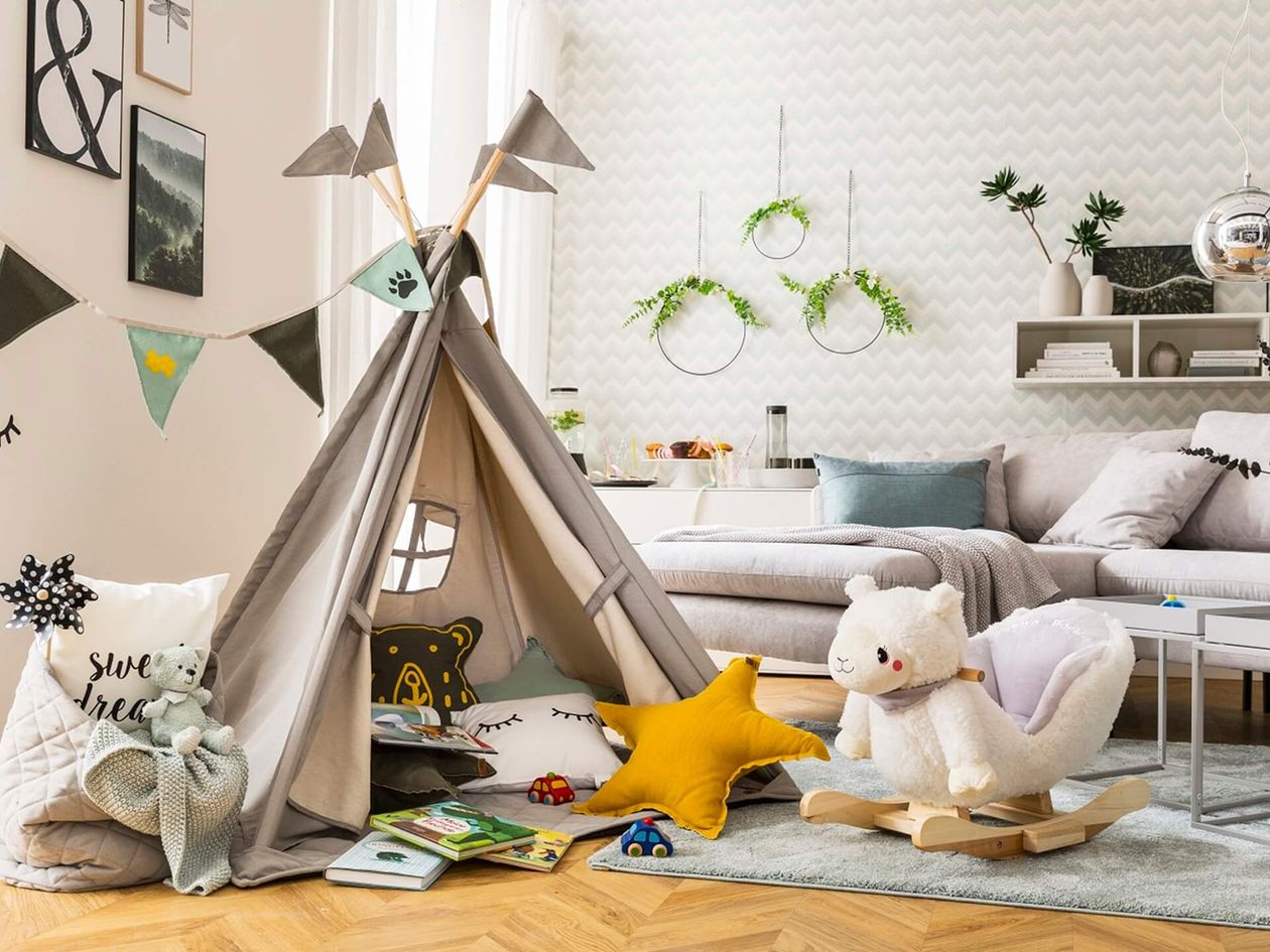 Gemütliche Wohnzimmerecke mit Tipi-Zelt und vielen Kissen, Holz-Schaukel und bunten Details, ideal für eine Kinderspielecke.