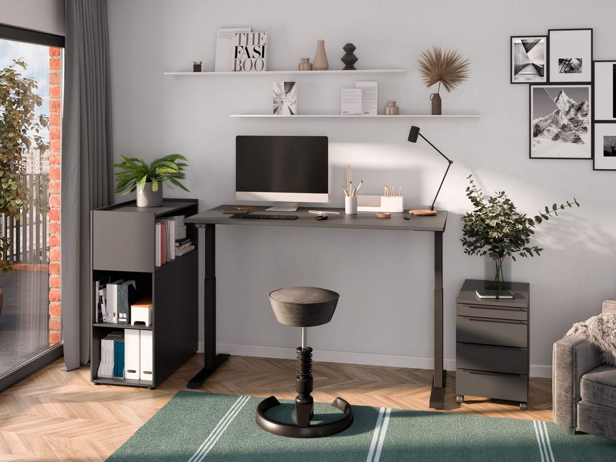 Helles Dachgeschossbüro mit großem Fenster, höhenverstellbarem Schreibtisch aus Holz, schwarzem Bürostuhl, Pflanzen und moderner Einrichtung.