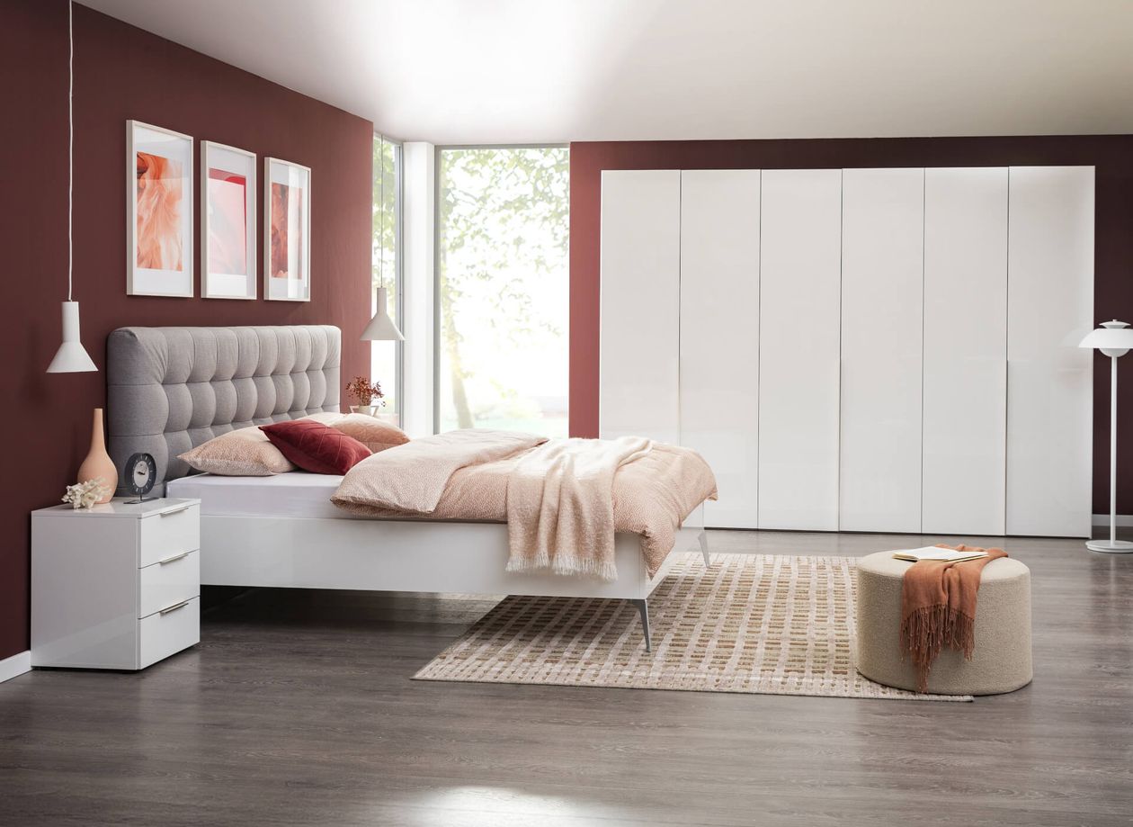 Modernes Schlafzimmer mit Holzmöbeln, grauem Kopfteil, dekorativen Kissen und Pflanzen. Fenster mit Blick auf die Natur, Hängelampe.