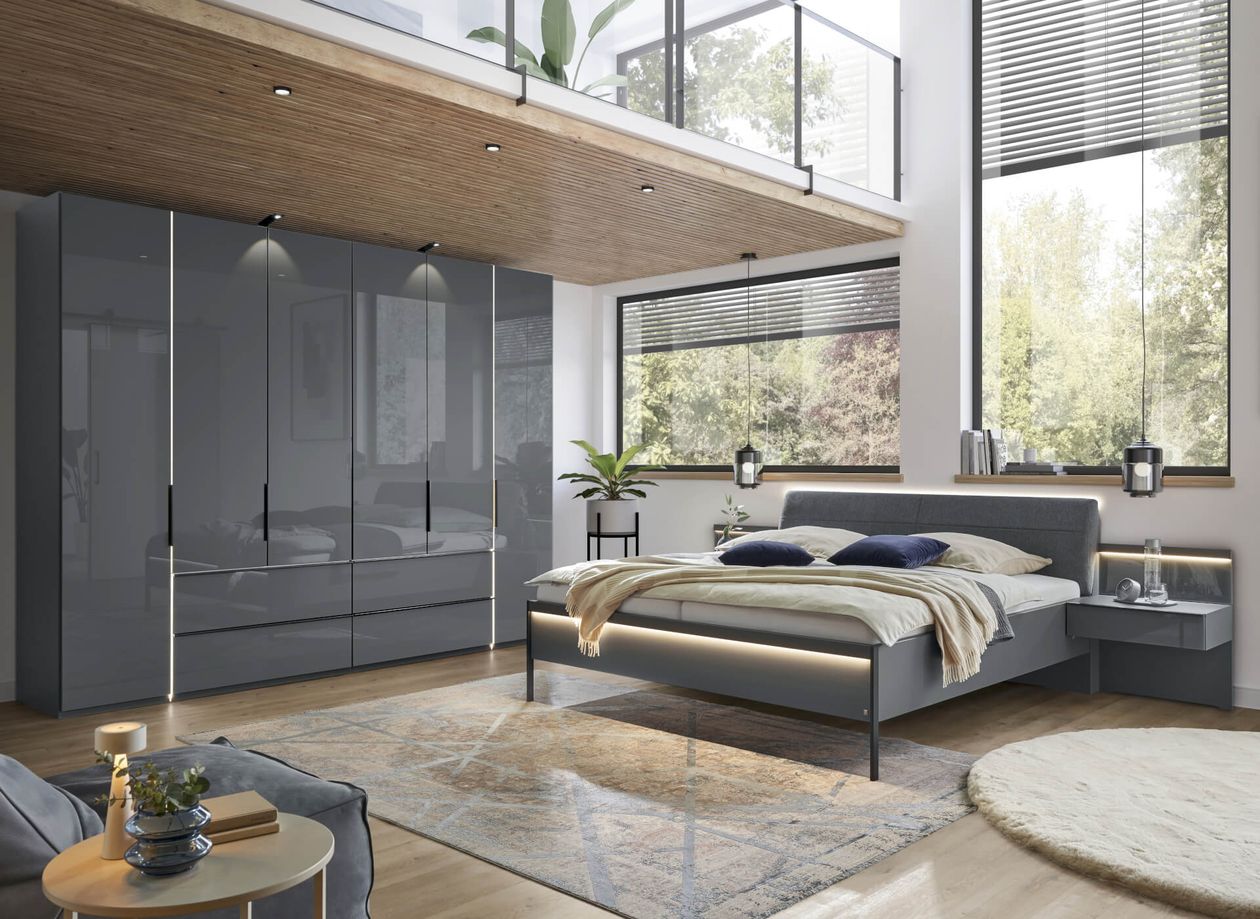 Modernes Schlafzimmer mit einem Bett aus Holz, grünen und grauen Decken, einem abstrakten Kunstwerk an olivgrüner Wand und einem Holzschrank.