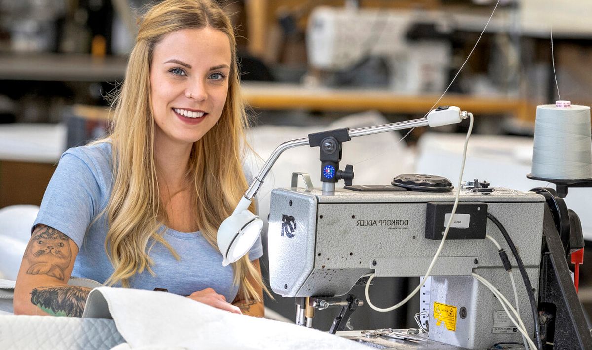 Frau an Nähmaschine lächelt in die Kamera.