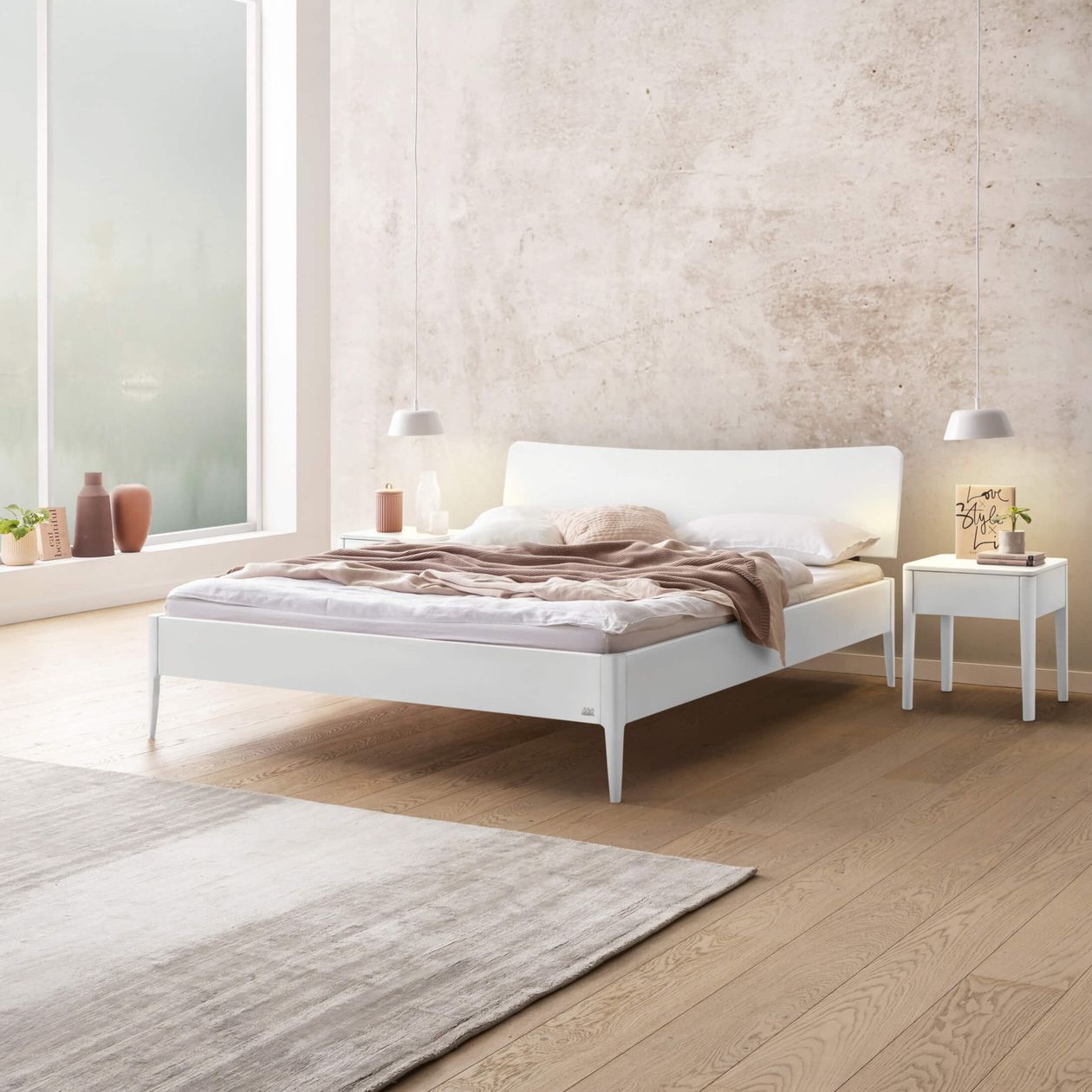 Ein minimalistisches Schlafzimmer mit einem weißen Bett, einer beigen Decke und einem Beistelltisch. Sanfte Beleuchtung und ein großes Fenster sorgen für eine ruhige Atmosphäre.