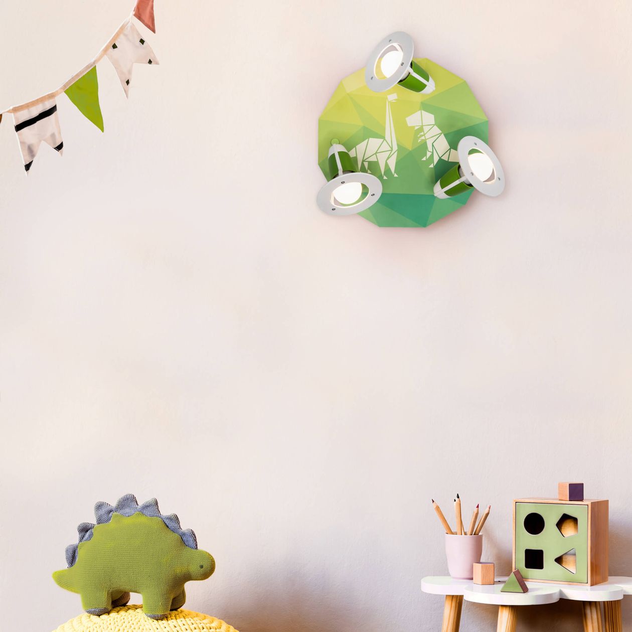 Kinderzimmer mit grüner Dinosaurier-Lampe an der Wand, einem kleinen Tisch mit Holzspielzeug und Bleistiften, und einer Wimpelkette.