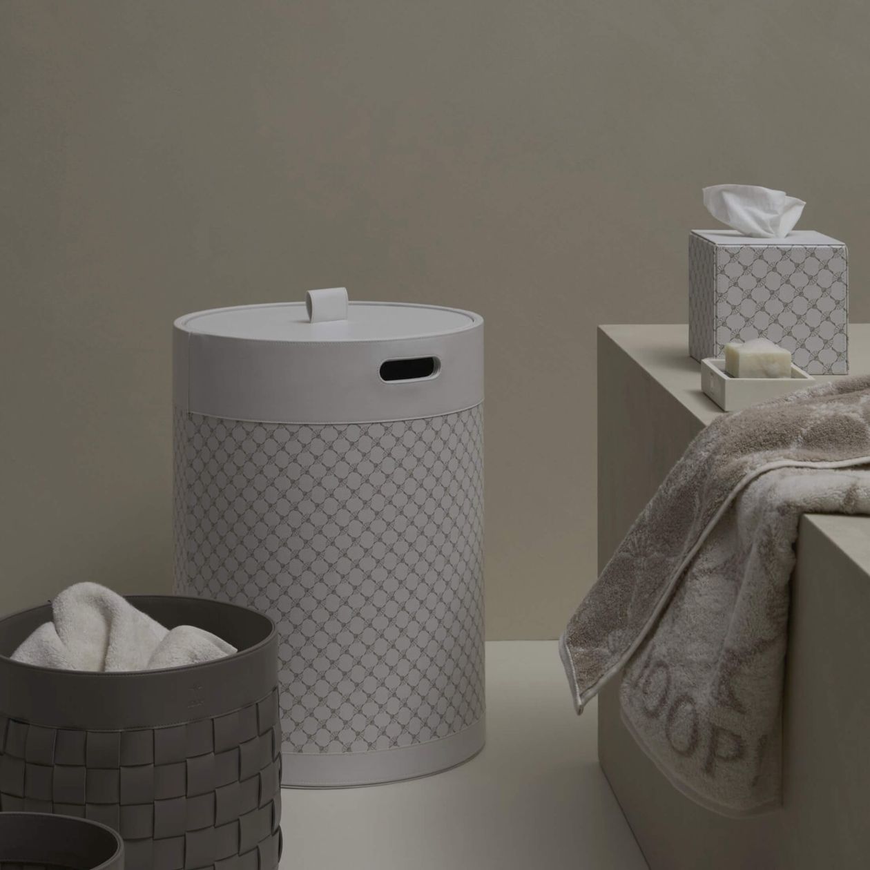 Grauer Wäschekorb, Handtuch, Taschentuchbox und geflochtener Korb in einem minimalistisch gestalteten Badezimmer.