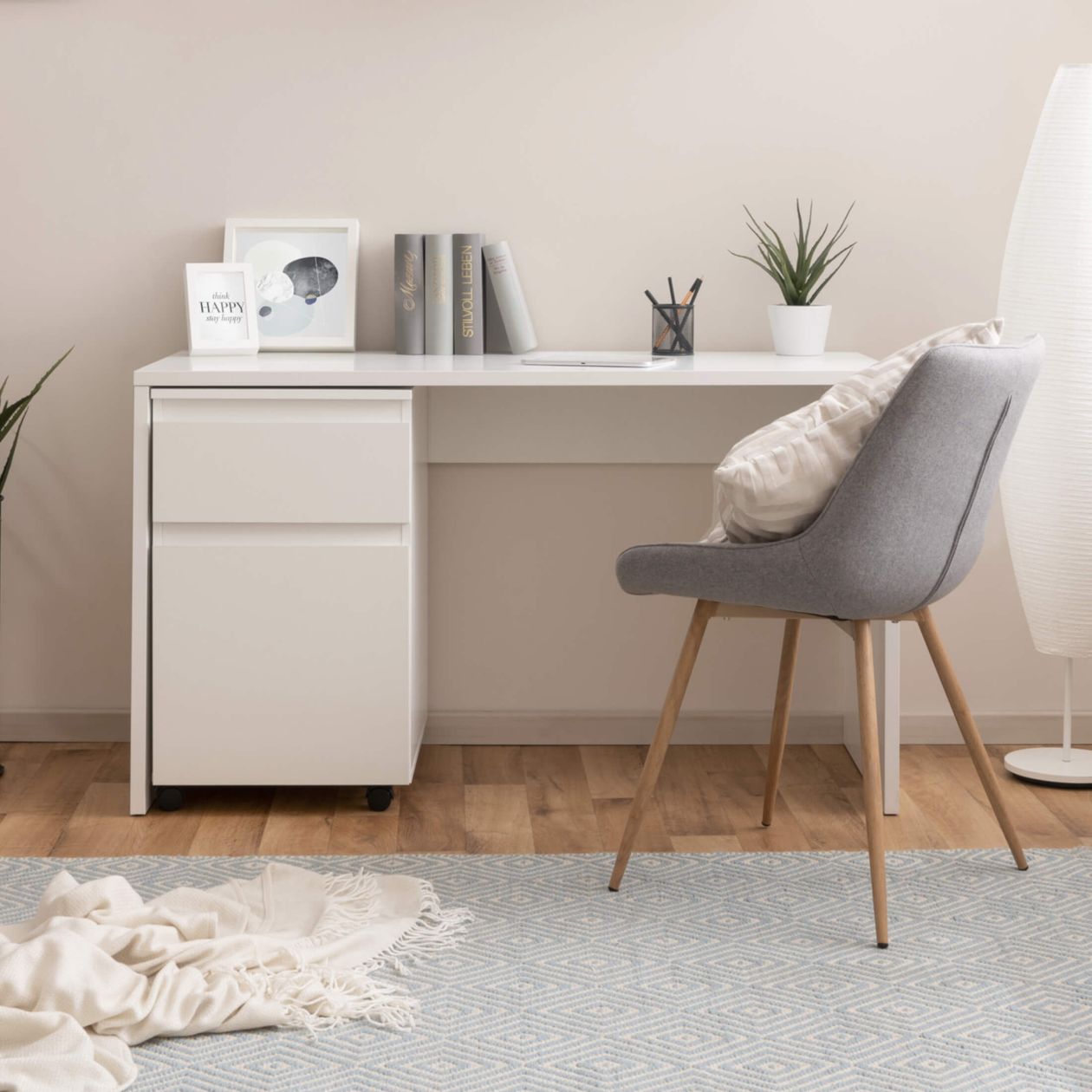 Minimalistischer Arbeitsplatz mit weißem Schreibtisch, grauem Stuhl, Pflanzen, Büchern und Dekorationen auf einem Holzfußboden mit blauem Teppich.