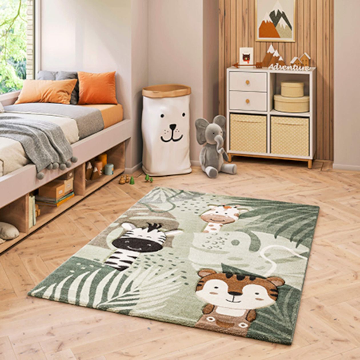 Kinderzimmer mit farbenfrohem Teppich mit Tiermotiven, Bett mit orangefarbenen Kissen, Kuscheltier-Elefant und Holzkommode auf Holzfußboden.