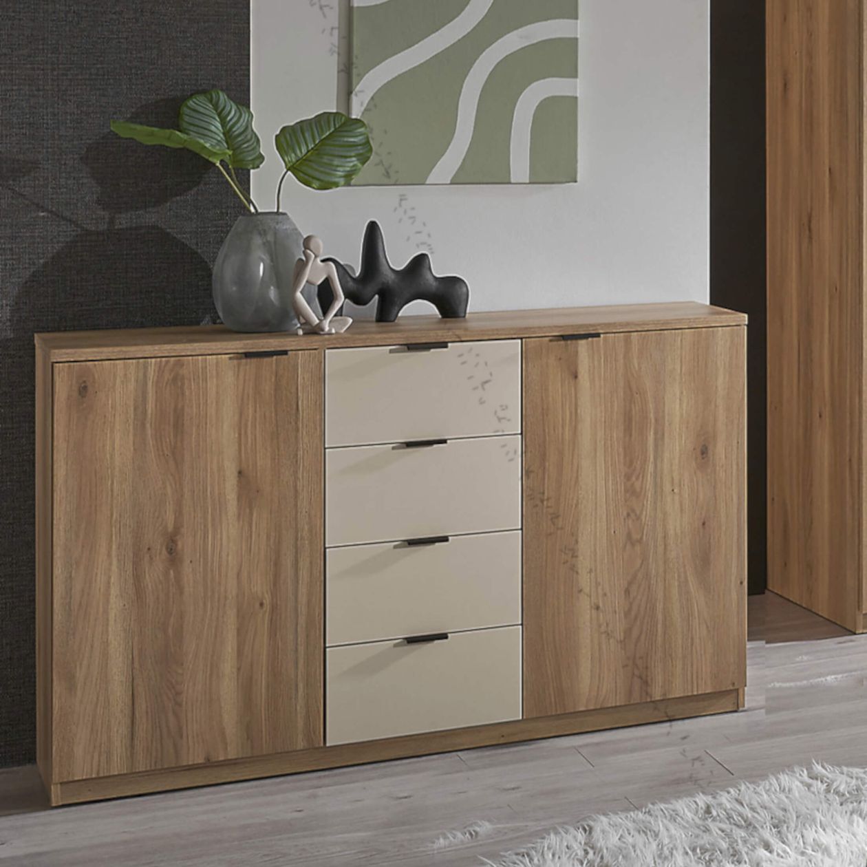 Holz-Kommode mit beigen Schubladen, dekoriert mit großer Vase, Pflanzen, Skulpturen und abstraktem Kunstwerk im Hintergrund.
