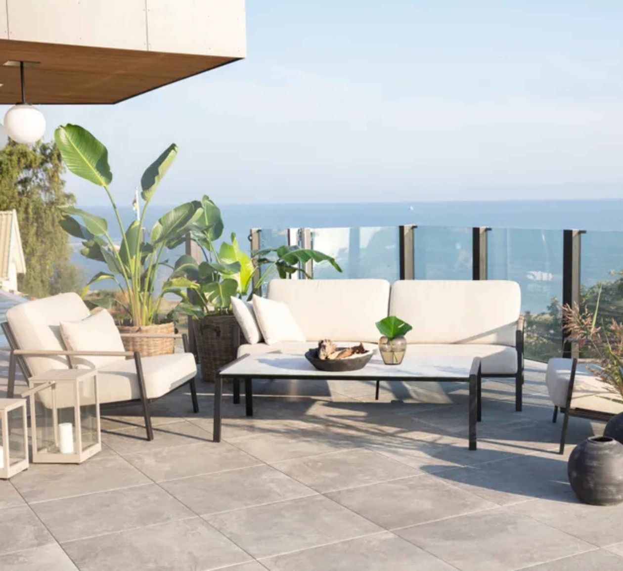 Moderne Terrasse mit weißen Möbeln, Pflanzen, Kerzenlaternen und Meerblick.