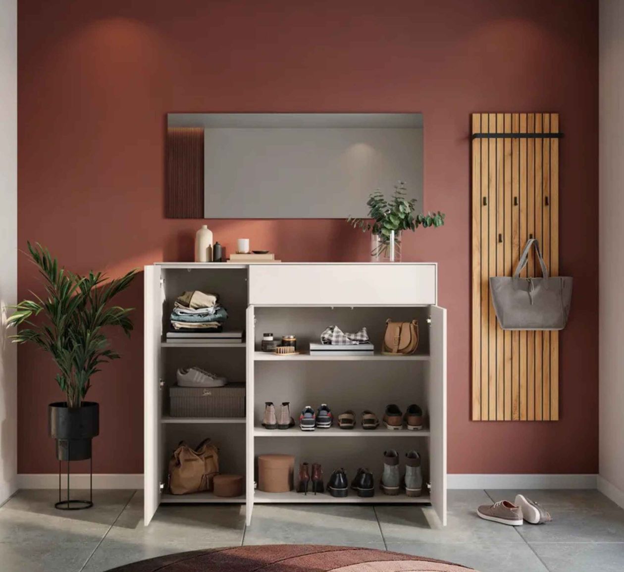 Moderner Flur mit rotbrauner Wand, einem weißen Schuhschrank, Spiegel, Pflanzen, Holzleistenkleiderhaken und Schuhen auf dem Boden.