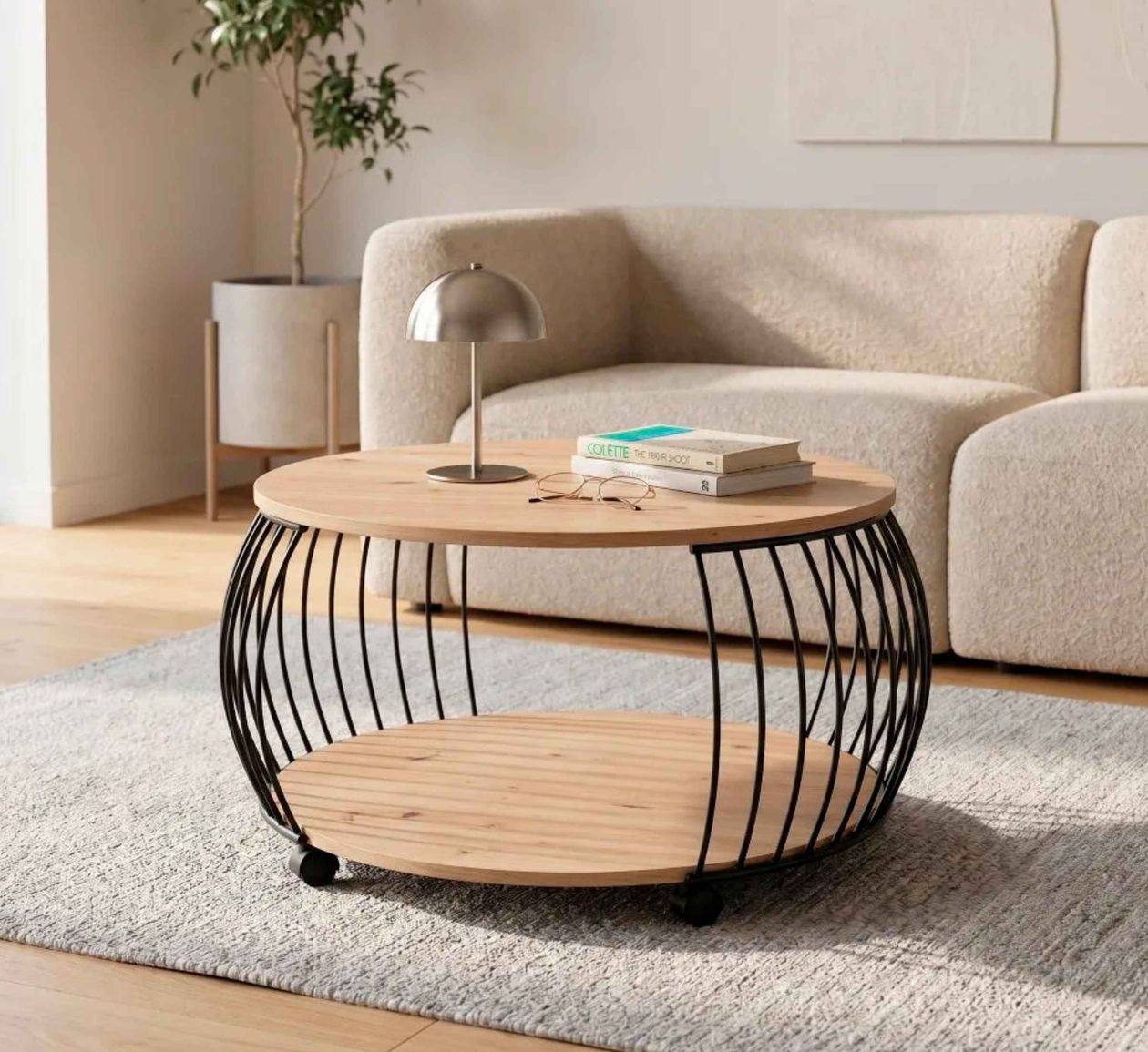Runder Couchtisch mit Holzplatte und schwarzem Metallgestell, darauf Tischlampe, Bücher und Brille. Heller Teppich und cremefarbenes Sofa im Hintergrund.