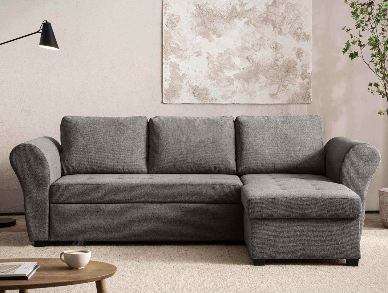 Graues Ecksofa mit weichen Kissen, stehend in einem modernen Wohnzimmer, umgeben von Lampe, Kunstwerk und Pflanze.