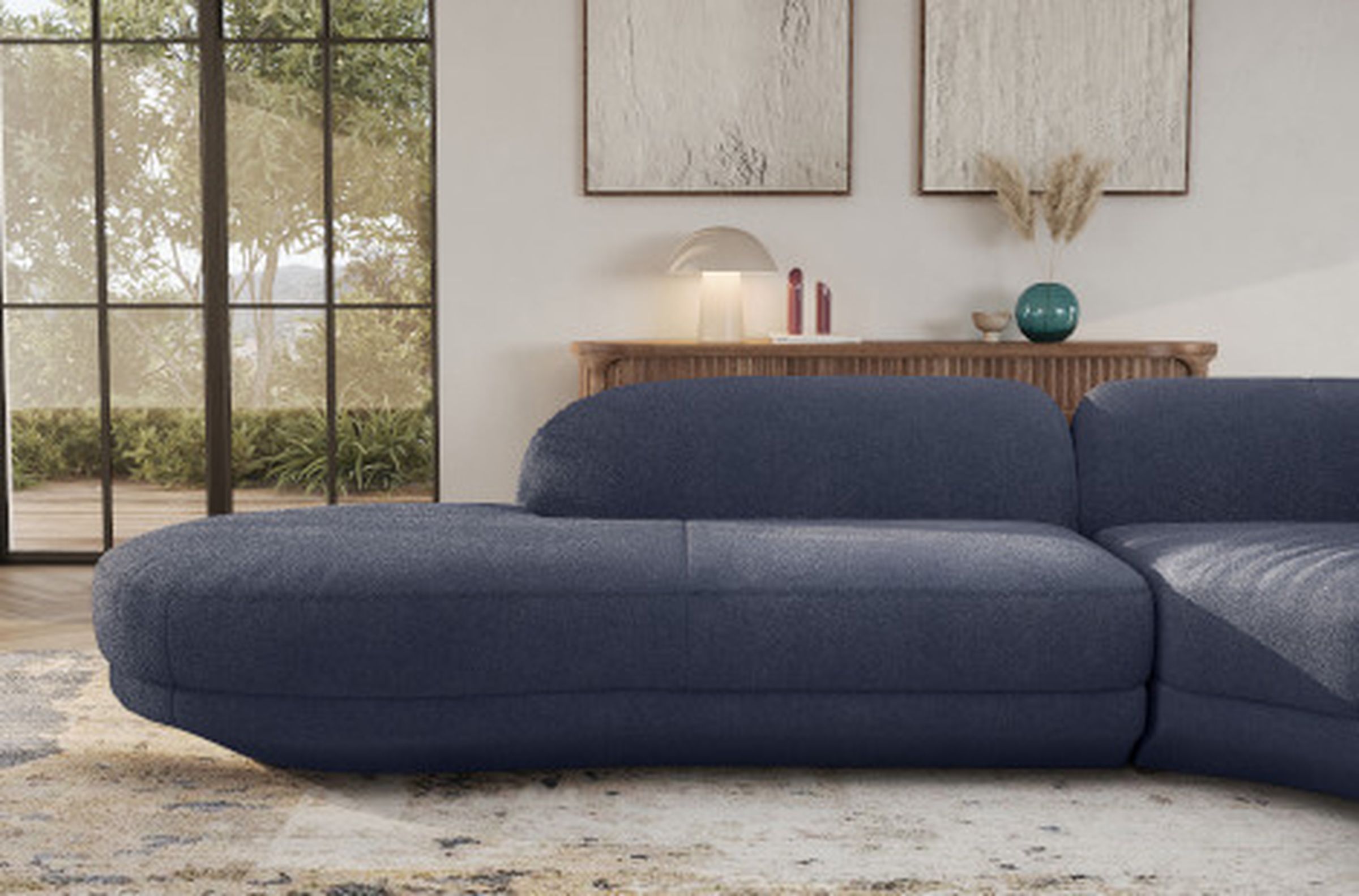 Ein modernes Wohnzimmer mit einem marineblauen Sofa, einem hölzernen Konsolentisch, Dekorationsgegenständen und großen Fenstern mit Blick auf das Grün draußen.