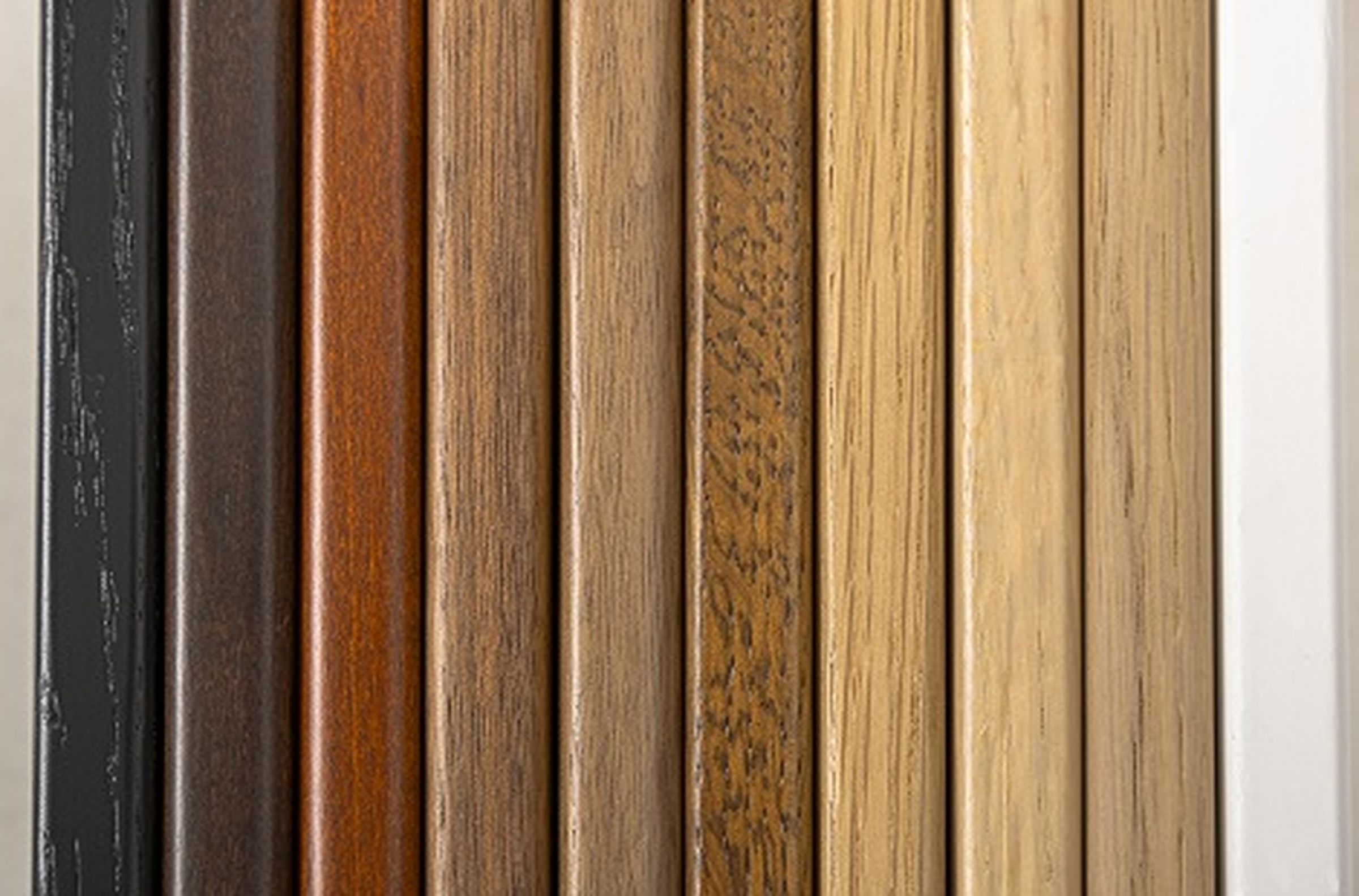 Eine vertikale Anordnung von Holzplanken in verschiedenen Farbtönen, von Dunkelbraun bis Hellbeige, die unterschiedliche Holzstrukturen zur Geltung bringt.