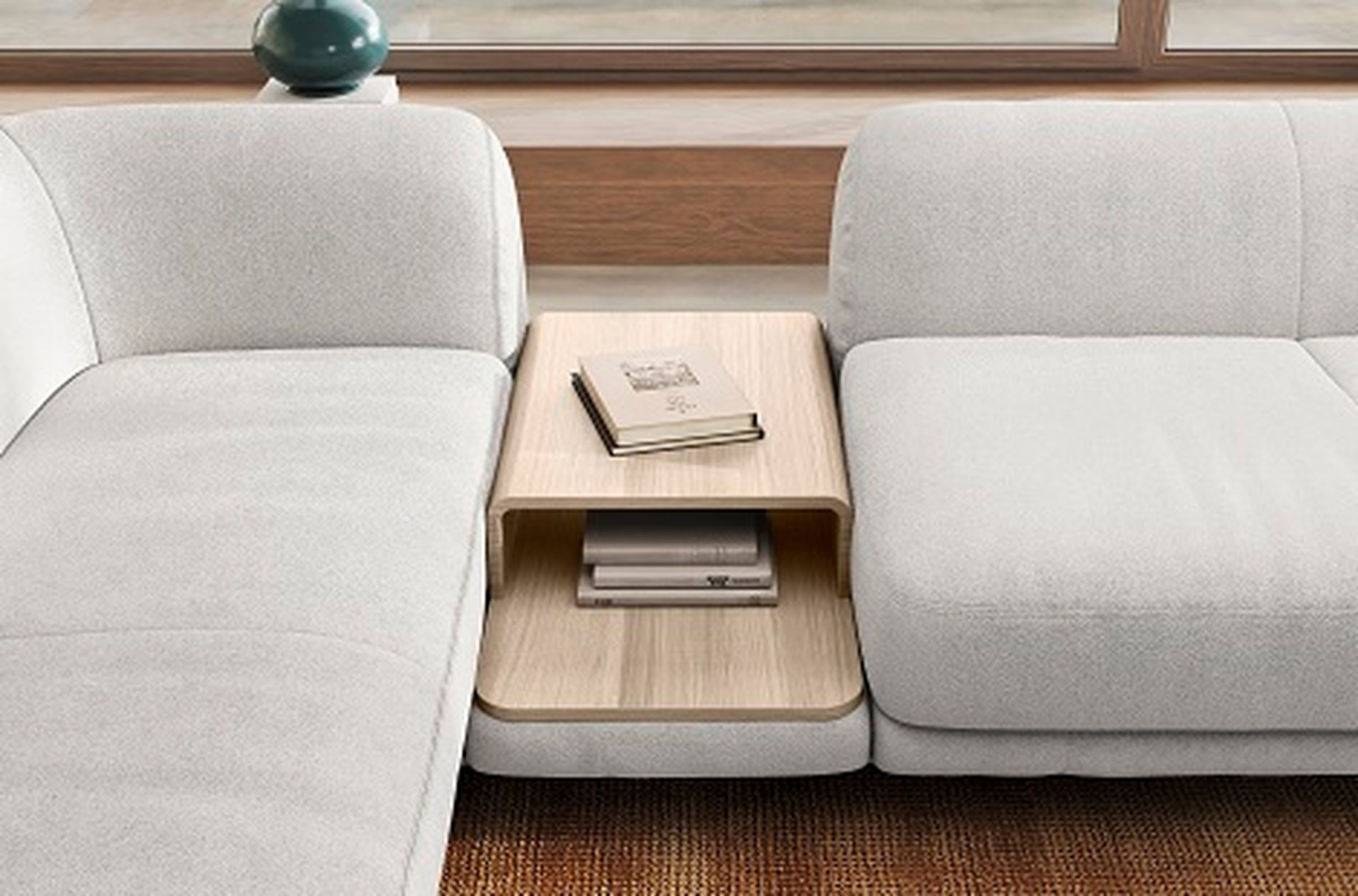 Modernes weißes Sofa mit einem hölzernen Beistelltisch in der Mitte, auf dem ein Buch und zwei gestapelte Zeitschriften auf einem gewebten Teppich liegen.
