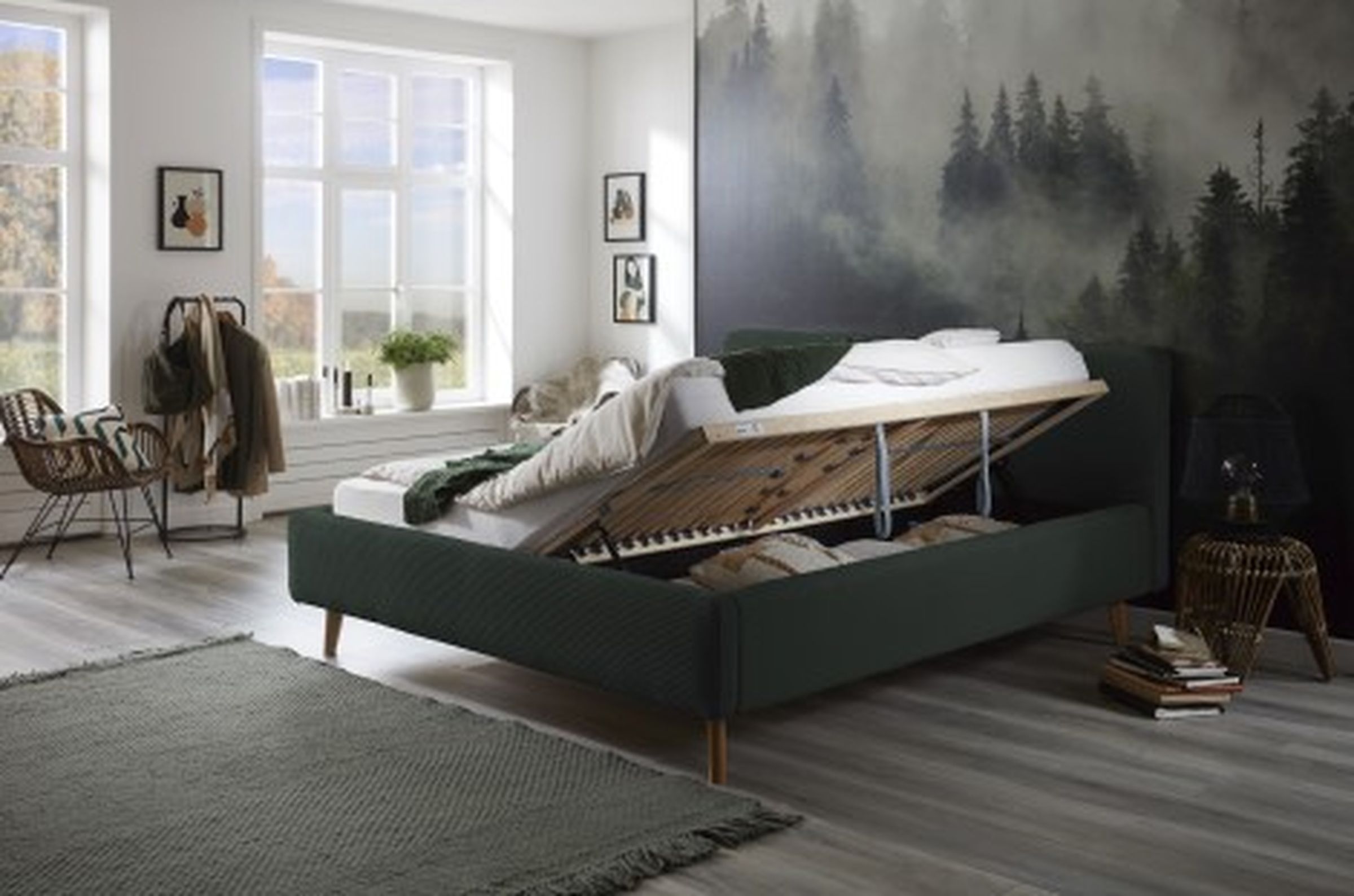 Polsterbett Mattis von meise.möbel aus dunkelgrünem Stoff in einem dunkel gehaltenem Schlafzimmer mit Naturtapete.