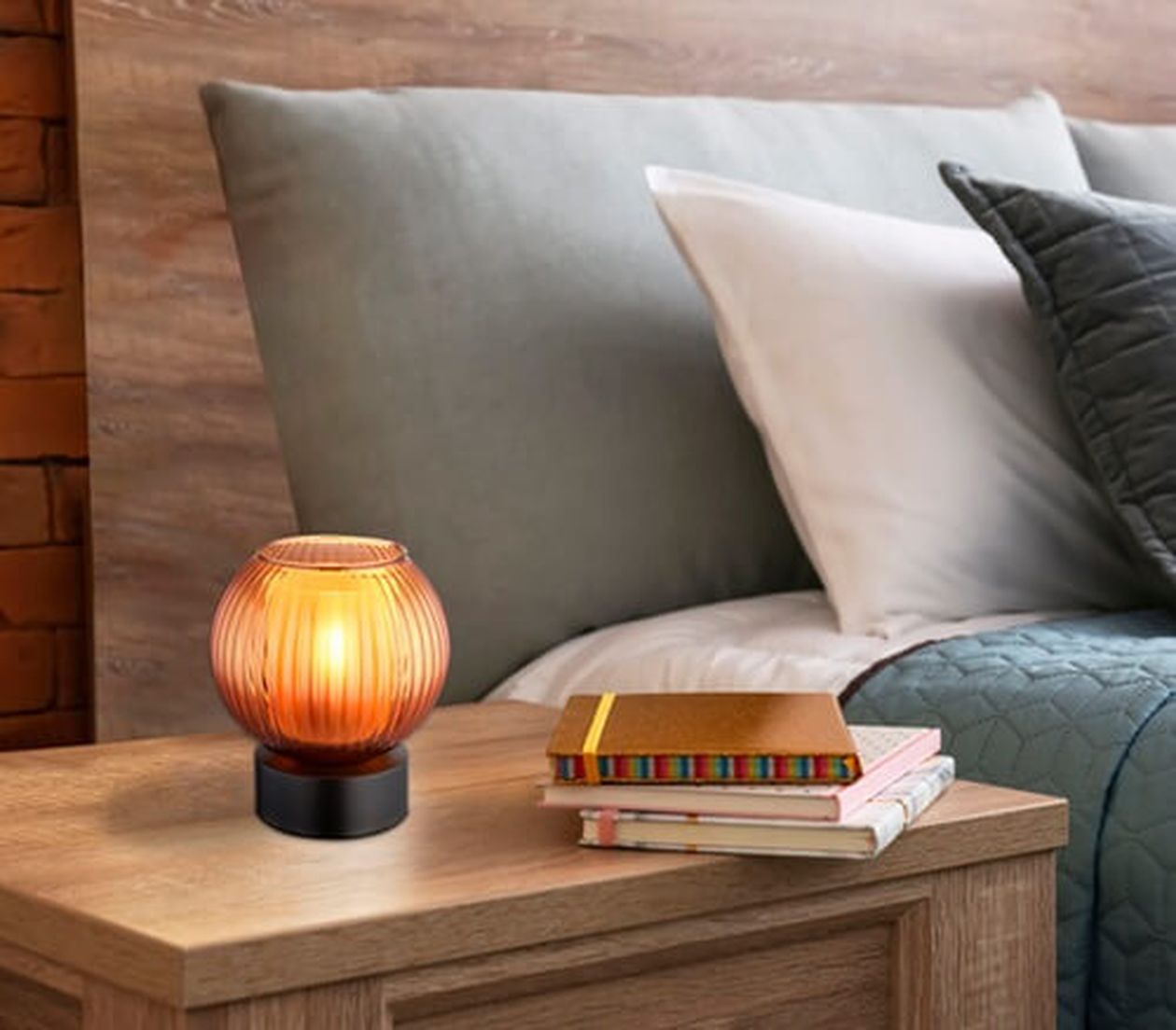 Eine gemütliche Schlafzimmerszene mit einem hölzernen Nachttisch, einer leuchtenden Bernsteinlampe und einem Stapel Bücher, neben einem ordentlich gemachten Bett mit Kissen.
