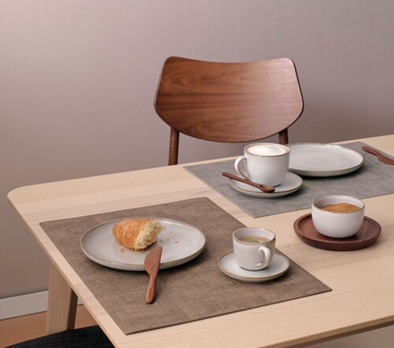 Beiger Tischset auf einem Esstisch, gedeckt mit einem Croissant und Heißgetränken. Der Fokus liegt auf schlichter, moderner Tischdekoration.