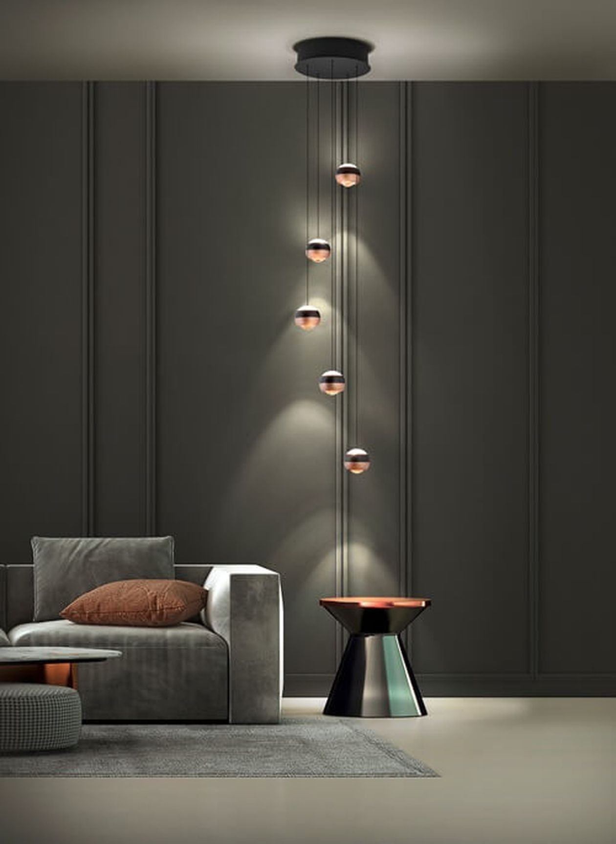 Modernes Wohnzimmer mit einem grauen Sofa, braunen Kissen, hängenden kugelförmigen Lichtern, einem kleinen Tisch und einem strukturierten Teppich auf hellem Boden.