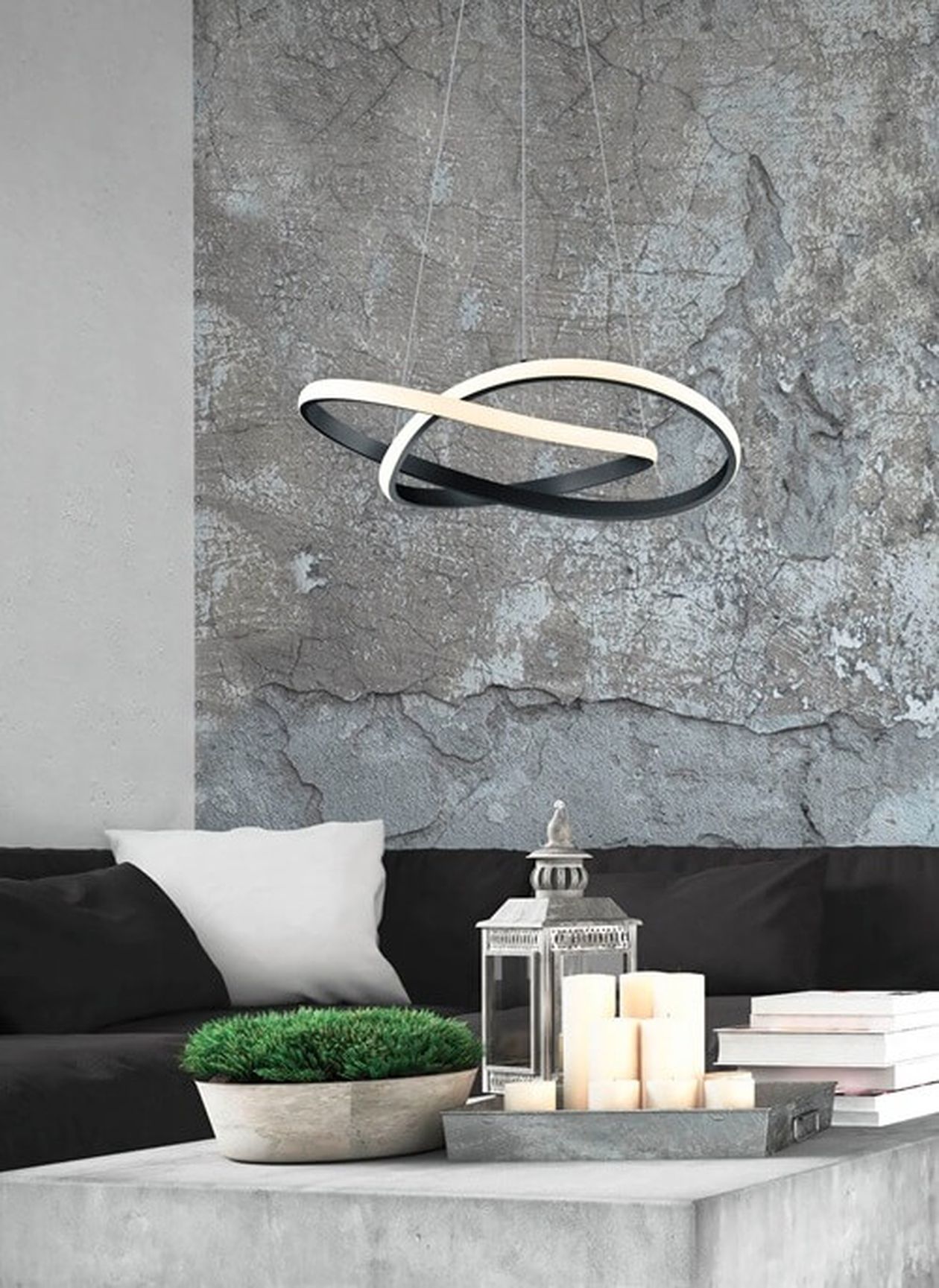 Modernes Wohnzimmer mit einer geometrischen Hängelampe, einer strukturierten grauen Wand, einem schwarzen Sofa, weißen Kissen, Kerzen, einer Laterne und einer Topfpflanze.